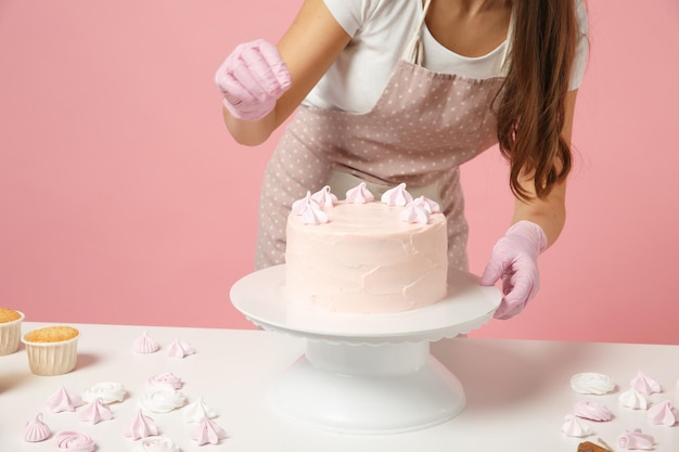 Close up cropped chef cook confectioner baker in apron white t-shirt cooking at table isolated on pink pastel background in studio. Cake decorating process strawberry meringue. Mock up food concept.