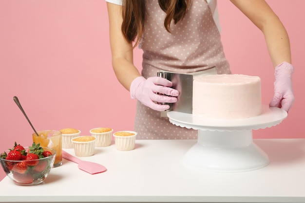 Close up cropped chef cook confectioner or baker in white t-shirt cooking at table isolated on pink pastel background in studio. Cream application cake making process. Mock up copy space food concept.