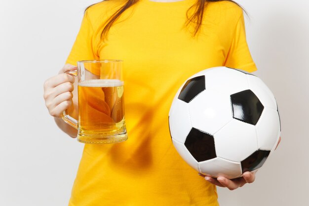 Close up cropped european young woman, football fan or player\
in yellow uniform holding pint mug of beer, soccer ball isolated on\
white background. sport, play football, healthy lifestyle\
concept.