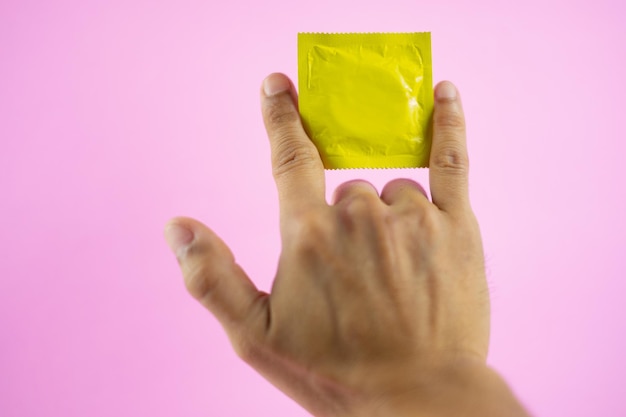 Foto close-up di una mano tagliata che tiene un pacchetto di preservativi contro uno sfondo rosa