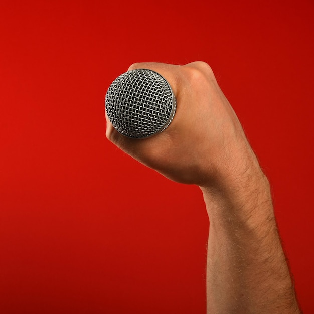 Photo close-up of cropped hand holding microphone against red background