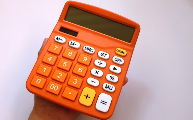 Close-up of cropped hand holding orange calculator against white background