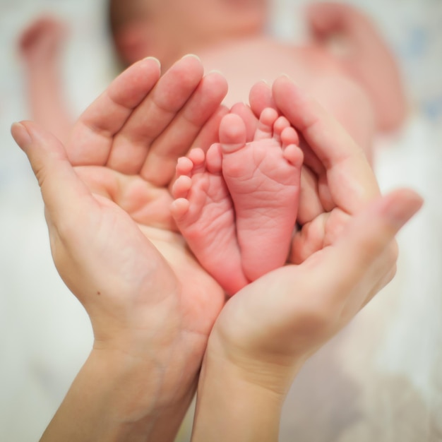 Foto close-up di mani tagliate che tengono i piedi di un neonato a casa