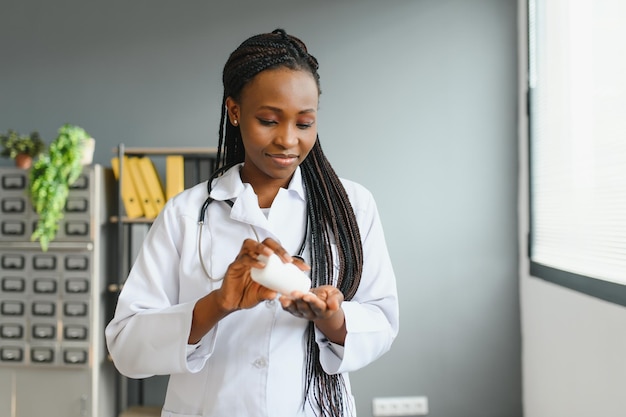 Крупный план обрезанного горизонтального снимка улыбающейся африканской женщины-врача или фармацевта, держащей красочные волдыри с таблетками, показывающей их на камеру, стоя в аптеке или больнице