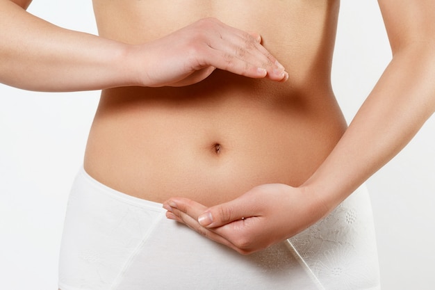 Close up cropped photo of beautiful woman's slim stomach, using hands she is showing a balance. The concept of healthy eating, diet. Early pregnancy. on white