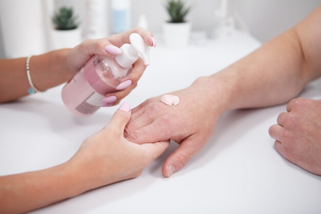 Close up cropped shot of professional manicurist using hand cream on male clients hands