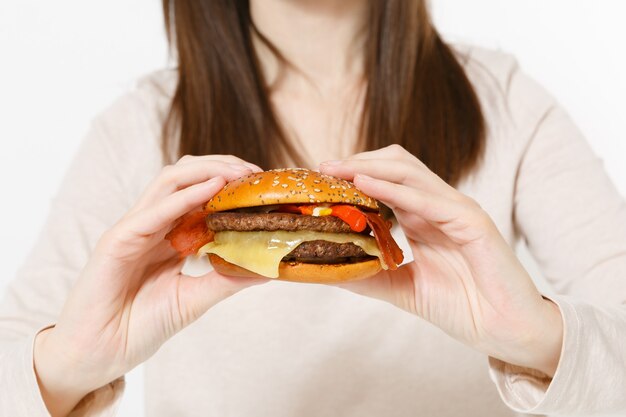 Close up cropped shot young woman in light clothes holding in hands burger isolated on white background. Proper nutrition or American classic fast food. Copy space for advertisement. Advertising area.