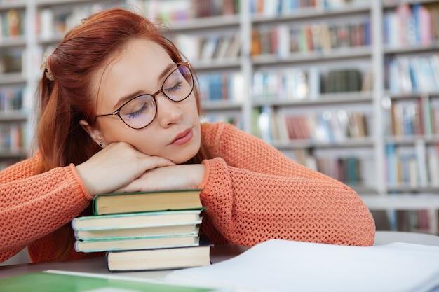 図書館で本の山で寝ている若い女性のトリミングされたショットを閉じる