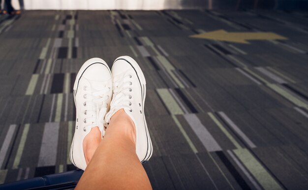 Close up crossed leg wear white sneaker lay on suitcase at airport terminal