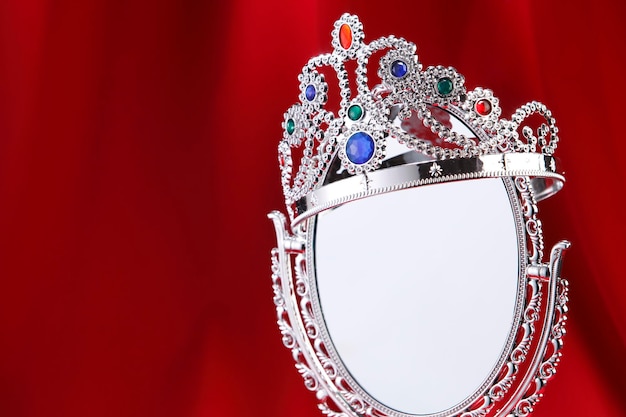 Photo close-up of crown over mirror on red fabric