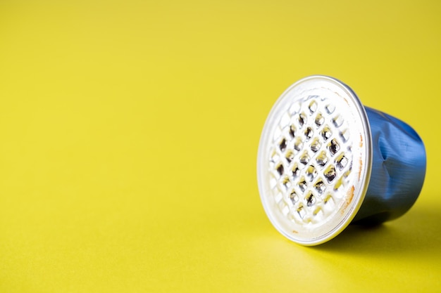 Close-up of a crumpled used aluminum coffee capsule on a yellow background. Blue color, recycling, side view, copy space