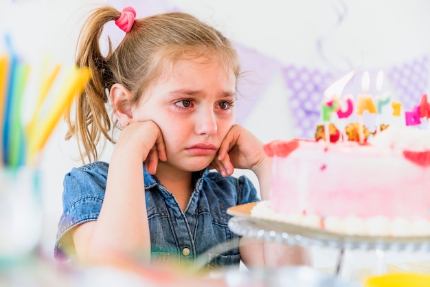 Foto primo piano di una ragazza che piange guardando la torta di compleanno