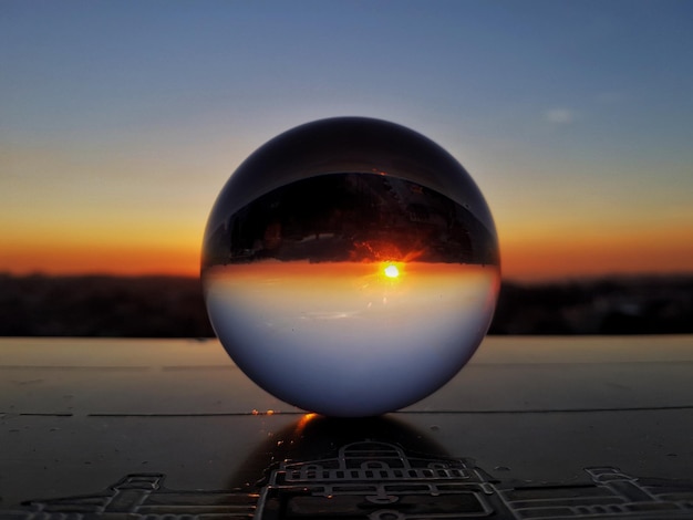 Photo close-up of crystal ball on landscape against sunset sky
