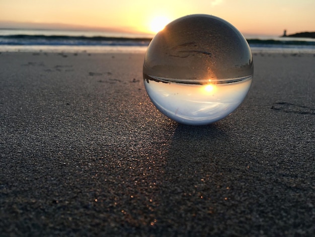 close-up of crystal ball on sand at beach during sunset