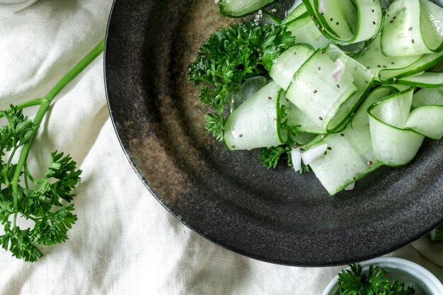 Закройте салат из огурцов и семян чиаса и лист зеленой петрушки в черной тарелке