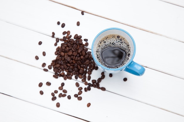 Close-up of a cup of coffee  and beans on white wooden table