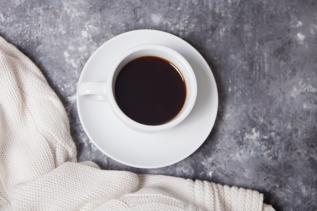 Close up of cup of coffee and knittead white plaid on the gray 