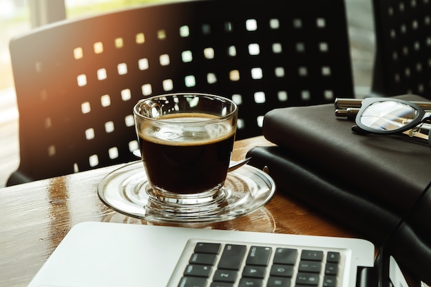 Close up of a cup of coffee and office supplies on desk in office at morning, warm tone