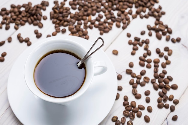 Close up of cup of coffee a saucer and a spoon with beans on the desk