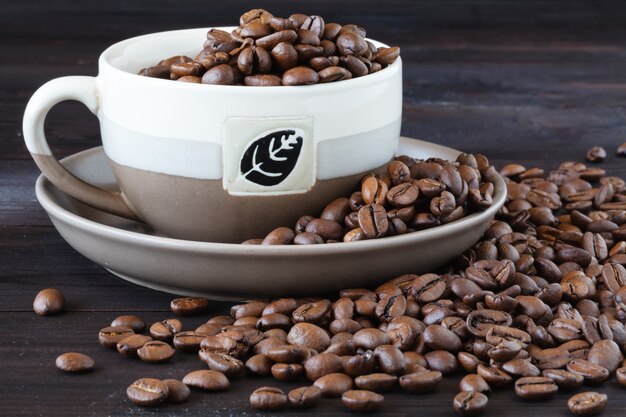 Foto chiuda in su della tazza di caffè espresso con i fagioli freschi su una tabella di legno