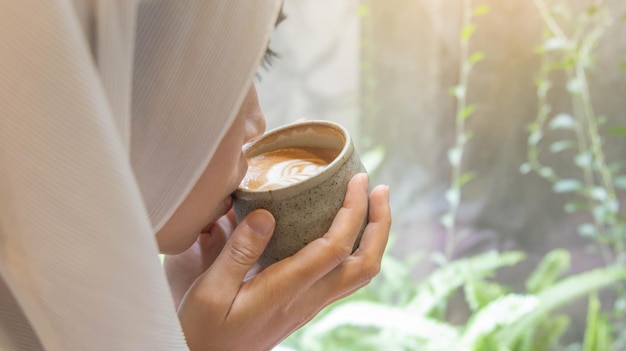 写真 コーヒー ショップでコーヒー カフェラテのカップを閉じる花形のラテ アート泡とコーヒー カップのカップを保持している女性の手