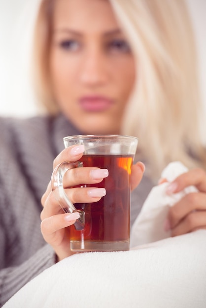 Close-up cup of tea held by the hand of girl, with a face out of focus, dressed in wool sweater, tucked in a blanket