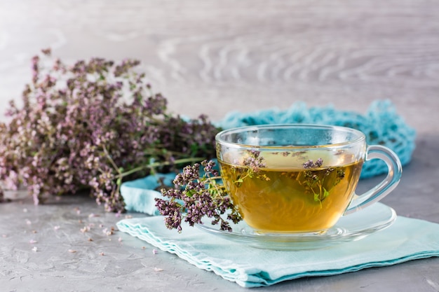 Close up on cup of tea with oregano and a dry bunch of herbs nearby