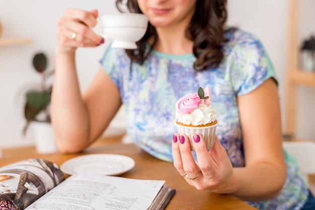 手にカップケーキとお茶のクローズアップ。キッチンの女性が自家製カップケーキで1時間を飲む