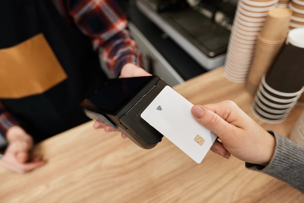 Foto primo piano, mano del cliente che tiene la carta di credito vicino al terminale nfc. il barista accetta il pagamento con carta di credito tramite la macchina pos nella caffetteria