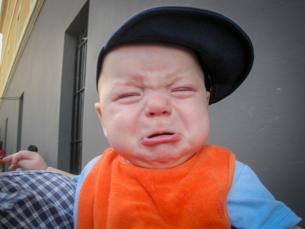 Photo close-up of cute baby boy crying against building