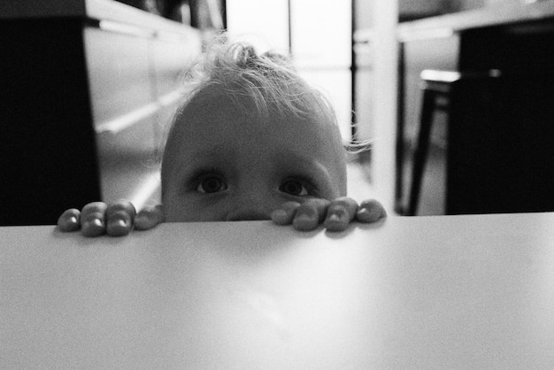 Photo close-up of cute baby girl looking up by table at home