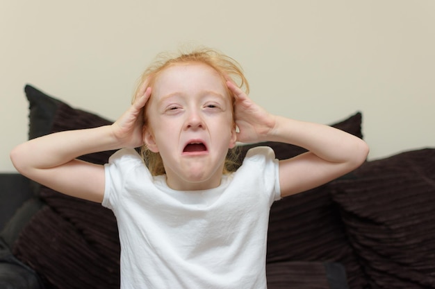 Photo close-up of cute girl crying while sitting on sofa at home