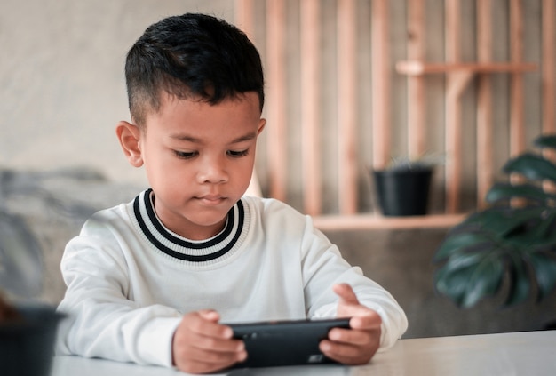 Close up of cute little 4s Caucasian boy child look at cellphone screen play online game on gadget.