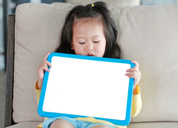 Close up Cute little child girl holding empty white blackboard on fabric sofa