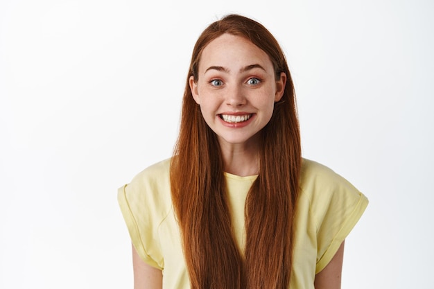 Close up of cute redhead girl smiling, looking hopeful and happy, anticipating something, glancing with hope and excitement, white background