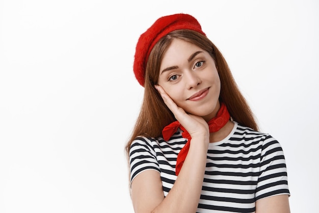 Close up of cute smiling girl in beret looking at front lovely, gazing with tender face expression, standing over white wall