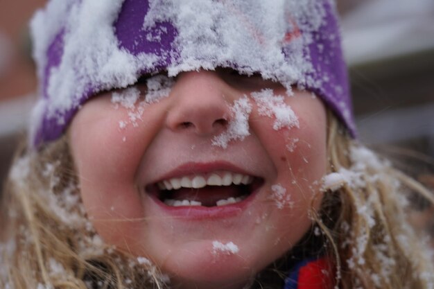 Foto close-up di una ragazza carina sorridente con la neve sul viso