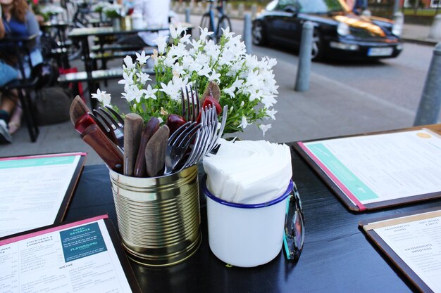 Close-up of cutlery in container by flowers at sidewalk cafe