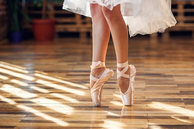 Close-up dancing legs of ballerina wearing white pointe ballet shoes in the dancing hall.