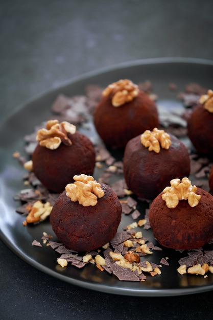 Close up on a dark plate of rum balls with wallnutsion dark table decorated with Autumn leaves.