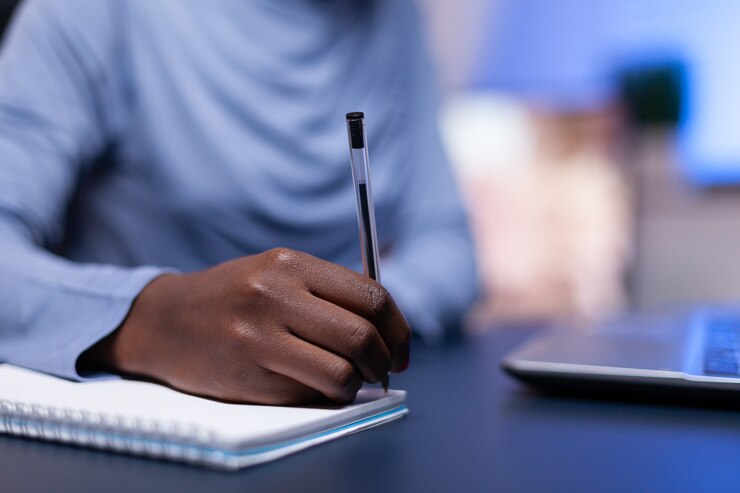 Photo close up of dark skinned woman taking notes while working from home office sitting at desk comp. black freelancer respecting deadline studying late at night.