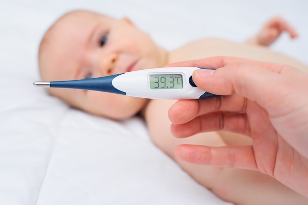 Close-up - de hand van een moeder of arts die een thermometer vasthoudt met een markering van 39,3 graden op de achtergrond van een huilende baby. Kinderziekten, hoge lichaamstemperatuur.