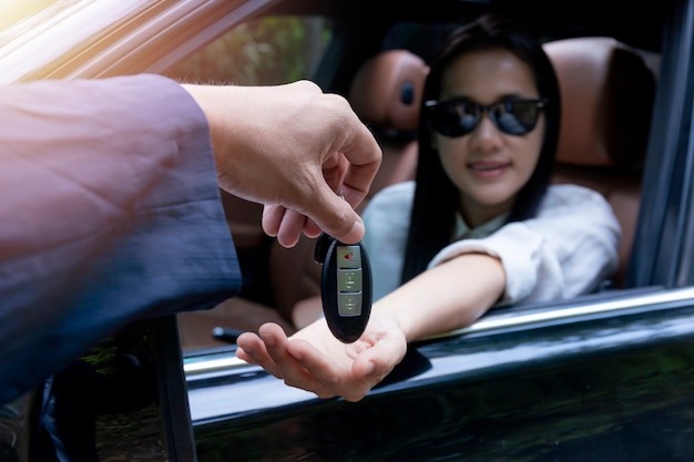 Close up of dealer giving key to new owner car. New car. Auto dealer giving woman automobile key for test drive on country road.