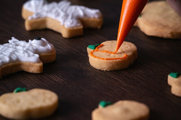 Close up of decorating cute Halloween pumpkin gingerbread cookies with frosting