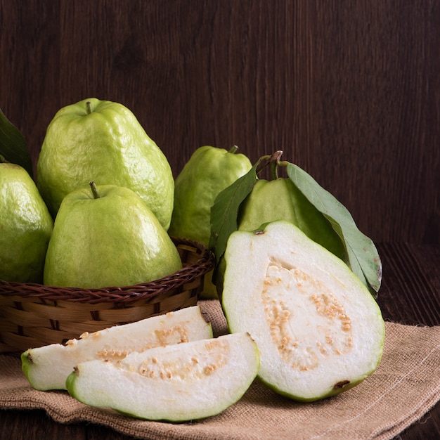 Close up of delicious beautiful guava set with fresh green leaves isolated on dark wooden table background.