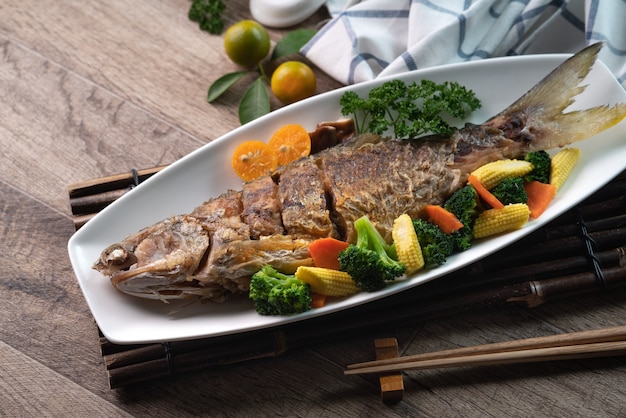 木製のテーブルの上に野菜と白いプレートでおいしい魚のフライパンのクローズアップ。