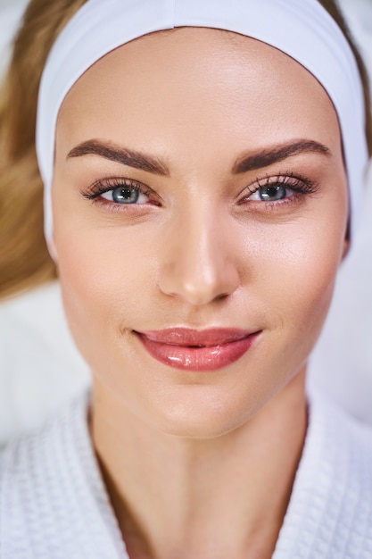 Close up of delighted young lady in bathrobe while she is spending good day in salon