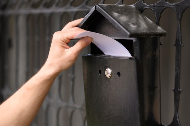 Close-up delivery man dropping envelope in the mailbox