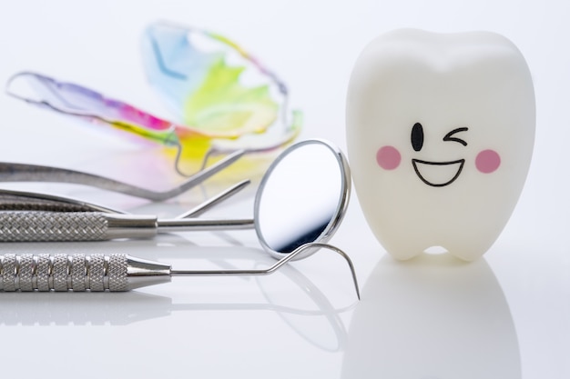 Chiuda su strumenti di dental e denti di sorriso modellano su fondo bianco.