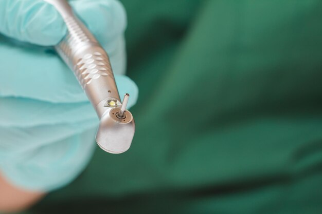 Close-up dentist's hand in a latex glove with high-speed dental handpiece on blurred background. Medical tools concept. Shallow depth of fiel.